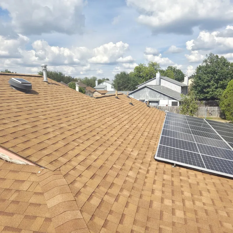 Solar panels on a tan shingle roof with neighboring houses behind
